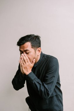 İçerideki koyu renk saçlı adam, koyu renk bir gömlek giyiyor ve elleriyle yüzünü kapatıyor. Kötü olabilir..