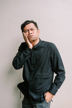 Dişi ağrıyan sıkıntılı bir adam, koyu mavi bir gömlek giyerken çenesini acı içinde tutuyor.