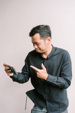 Asyalı adam telefonuna soru soran bir yüz ifadesiyle işaret ediyor. İnternette gördüklerinden emin değil gibi.