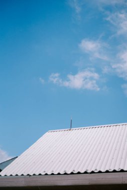 Açık mavi gökyüzüne karşı bükülmüş metal bir çatının minimalist görüntüsü.