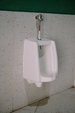 Umumi tuvaletteki benekli fayans duvarındaki beyaz pisuvarı kapat. Tesisat ve fikstür detaylarına odaklan. Yararlı banyo ekipmanlarıyla iç tasarım.