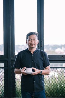 Modern odada kahveyi seven, gülümseyen ve huzurlu hisseden bir adam. Kentsel alanda bir dinlenme anı. 