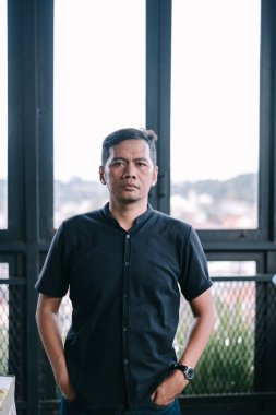 Sıradan giyinmiş olgun bir Asyalı 'nın portresi. Şehir arkaplanıyla kameraya özenle bakıyor..