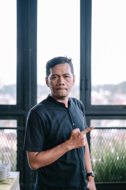 Kendine güveni tam adam parmağını gösteriyor. Modern pencere arkaplanına karşı ciddi ifade portresi. Yön gösterme veya bir noktaya değinme