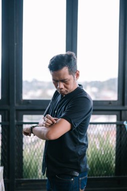 Düşünceli bir adam bir pencerenin yanında kollarını sıvar. Doğal ışık, düşünme anını güçlendirir.