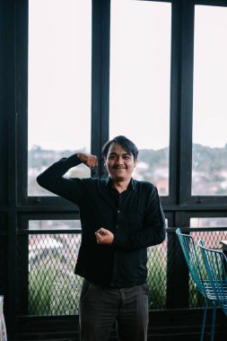 Modern ve hafif bir çalışma alanında kaslarını esneten mutlu genç bir adamın portresi. Güven ve başarı göstergesi.