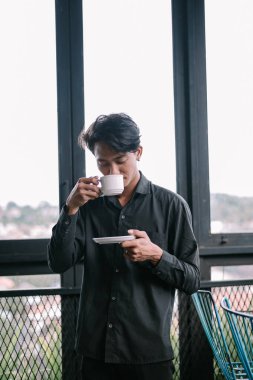 Düşünceli genç adam pencerenin yanında sıcak bir içecekten hoşlanıyor..
