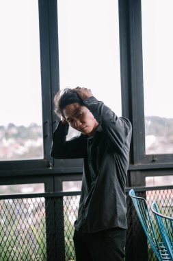 Derin düşüncelere dalmış düşünceli genç Asyalı bir adam pencerenin yanında duruyor..