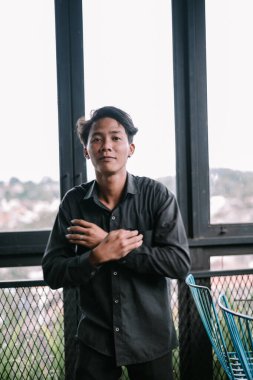 İçerideki pencerenin yanında duran düşünceli Asyalı bir adamın portresi. Kendine güvenen havalı ve modaya uygun bir genç.