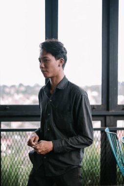 Siyah tişörtlü dalgın genç bir adam üzüntülü bir şekilde pencereden dışarı bakar, düşüncelere dalmış..