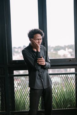 Dişi ağrıyan genç bir adam çenesini pencerenin yanında tutuyor. Yoğun diş ağrısı, sağlık sorunu kavramı