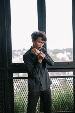 Gömleğin kollarını ilikleyen havalı Asyalı adam. Çekici ve stil sahibi, ciddi bir ifadeyle odaklanmış, modern bir erkeğin kapalı çekimleri.