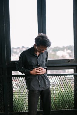 Karnı ağrıyan üzgün Asyalı bir adam pencerenin önünde dikiliyor.