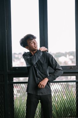 Arkasında şehir manzarası olan çağdaş bir apartman penceresinden bakan çekici bir genç adam. Olumlu duygular ifade etmek.