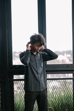 Yakasını düzelten düşünceli genç adamın kapalı bir portresi. Pencerenin yanında duran şık Asyalı adam.