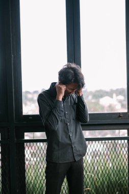 Sıkıntılı bir adam pencerenin yanında kulaklarını kapatır. Stres ve duygusal yükü tasvir eder.