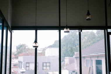 Şehir zeminine karşı kurulmuş eşsiz kolye ışıklarının yer aldığı bir pencereden atmosferik manzara. Tasarıma ve mahalle sahnesine odaklan.