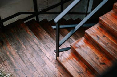Siyah metal korkuluklu, desenli ve tasarım elementlerini sergileyen rustik ahşap bir merdivenin yakın görüntüsü. Odunun sıcak renkleri, iç kısımlarına eski moda bir cazibe katıyor..
