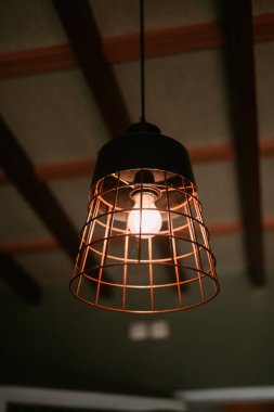 Modern bir kırsal evin içinde metalik bir kafes ile aydınlatılmış bir asma lambanın yakın çekimi..