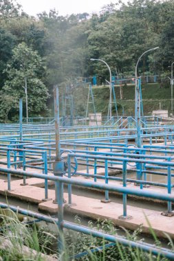 Yeşilliğe karşı karmaşık mavi boruları olan bir su arıtma tesisi. Endüstriyel altyapıyı ve su arıtma sürecini gösterir