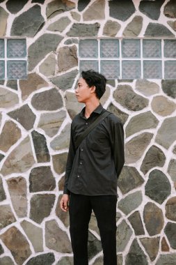 Taş duvara karşı genç adam portresi ve geometrik ızgara blok arka plan, başka tarafa bakıyor. Kendine güvenen ve modern stil.