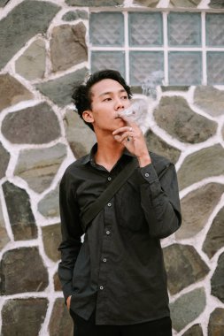 Genç bir adam sıradan bir ortamda sigara içiyor. Dalgın titreşimleri dokulu bir duvara yayıyor..