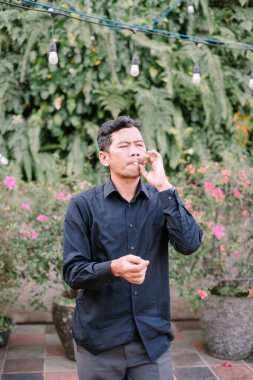 Rahat adam açık havada, yemyeşil ve sıcak ışıkların arasında sigara içmekten hoşlanıyor. Bir anlık duraksama ve düşünme.