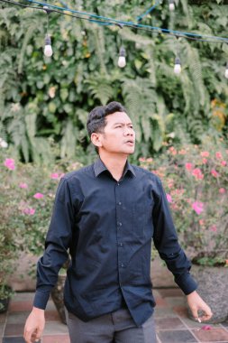 Adam yemyeşil bir bahçede, dekoratif sicim ışıklarıyla dalgın dalgın yukarı bakıyor.