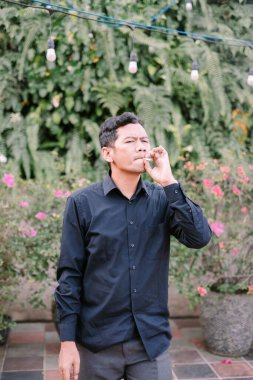 Düşünceli bir adam dışarıda sigara içmekten hoşlanır. O, yemyeşil bir bahçede sigara içerek rahatlıyor..