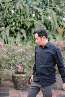 Çiçek açan güzel bitki ve ışıklarla dolu yemyeşil bir bahçede yürüyen ve düşünen bir adam.