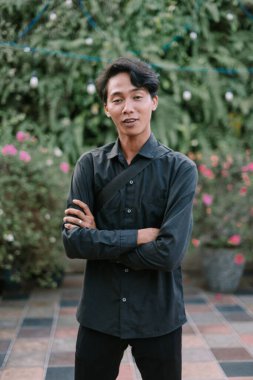 Bahçedeki genç adam kollarını kavuşturup kameraya bakıyordu. Doğal ışıkta çekilen.