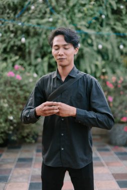 Genç Asyalı adam düşünceli meditasyonda, sakin bir ifadeyle, barışçıl doğanın tadını çıkarıyor.