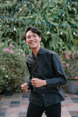 Neşeli genç bir adam bahçe ortamında gerçekten gülümsüyor. Pozitif enerji ve neşe dolu. Yaşam tarzı ve refah temaları için mükemmel