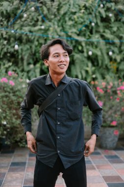 Açık havada mutlu bir yüzü olan genç bir adam. Günlük kıyafetler giyiyor ve omuz çantası var..