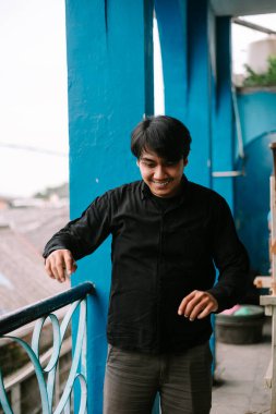 Neşeli bir adam mavi bir balkonda gülümsüyor, atmosferin tadını çıkarıyor. Mutluluk ve pozitiflik yayıyor.. 