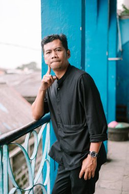 Asyalı bir adam derin derin düşüncelere dalmış, düşünceli bir bakışla balkonda duruyor.