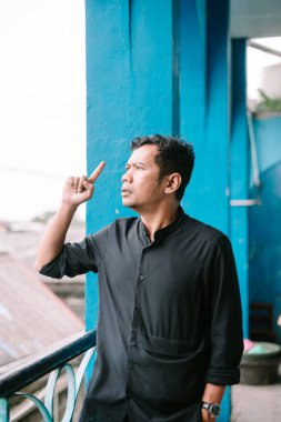 Balkonda duran bir adam yukarı bakıyor, düşünceli bir ifadeyle korkulukların ötesine bakıyor. Onun niyet bakışlarına odaklan.