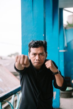 Asyalı bir adam kameraya yumruk atıyor. Nefsi müdafaa sırasında odaklanma ve kararlılık gösteriyor.