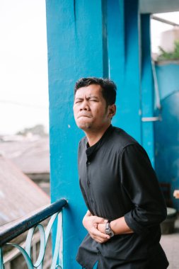 Karın ağrısı çeken Asyalı bir adam, karnını açık mavi balkonda rahatsızlık içinde tutuyor. Sağlık sorunu için illüstrasyon kavramı