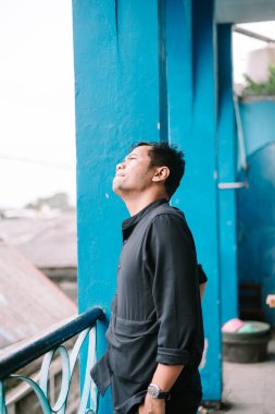 Düşünceli bir adam parlak mavi mimari bir arkaplan karşısında yukarı bakar. Düşünce ve iyimserlik hissini yakalar..