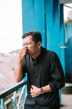 Asyalı adam suratını buruşturuyor, dışarıdaki kötü kokudan dolayı burnunu kapatıyor. Açık şehir ortamında tiksinme hissi..