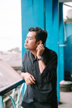 Siyah tişörtlü zarif bir adam düşünceye dalmış, mavi duvardan gözünü ayırmıyor. Sakin ve sessiz bir güven yayar..