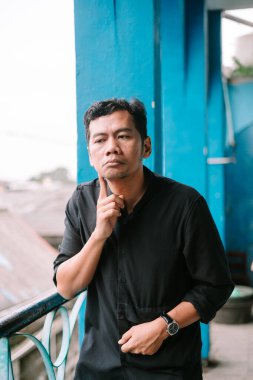 Dalgın Asyalı adam, canlı mavi arkaplana karşı düşünceli bir duruşta yakalandı.