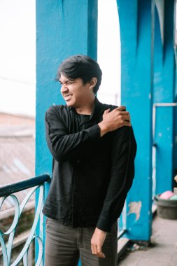 Stresli Asyalı adam aniden omuz ağrısı çekiyor. Mutsuz adam dışarıda omzunu tutmaktan acı çekiyor..