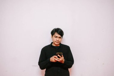 Asyalı bir adam telefonuna bakar. Yüzünde şaşkın ve şaşkın bir ifade vardır. Beyaz arka planda izole edilmiştir.