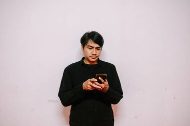 Asyalı bir adam telefonuna dikkatlice bakar, beyaz bir arka planda izole bir şekilde. Günlük yaşamda modern teknoloji.