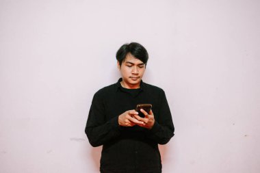 Siyah gömlekli genç adam akıllı telefonunu kullanıyor. Sade arkaplanda stüdyo çekimi