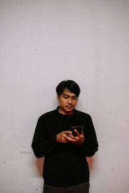 Koyu renk elbiseli Asyalı bir adam akıllı telefonunu kullanıyor. Konsantre ifade. Modern iletişim. Boş arkaplan. 