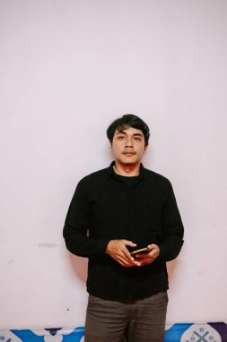 Düşünceli bir adam cep telefonunu parlak bir duvara dayayıp kameraya bakıyor.