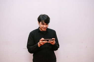 Genç adam akıllı telefonuyla bir oyuna daldı. Telefonu kullanırken odaklanmış ve mutlu..